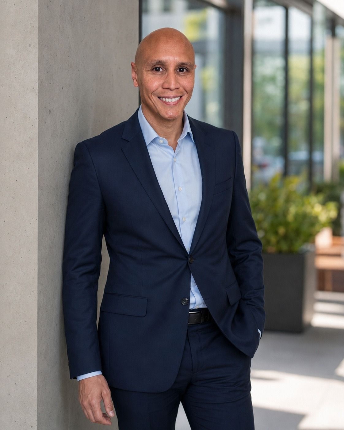 Brian Skyberg, smiling, in a navy suit and light blue shirt, leaning against a concrete wall outdoors